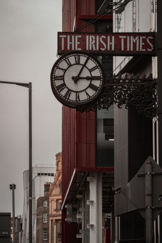 An urban scene featuring a classic clock and The Irish Times signage on a downtown street.